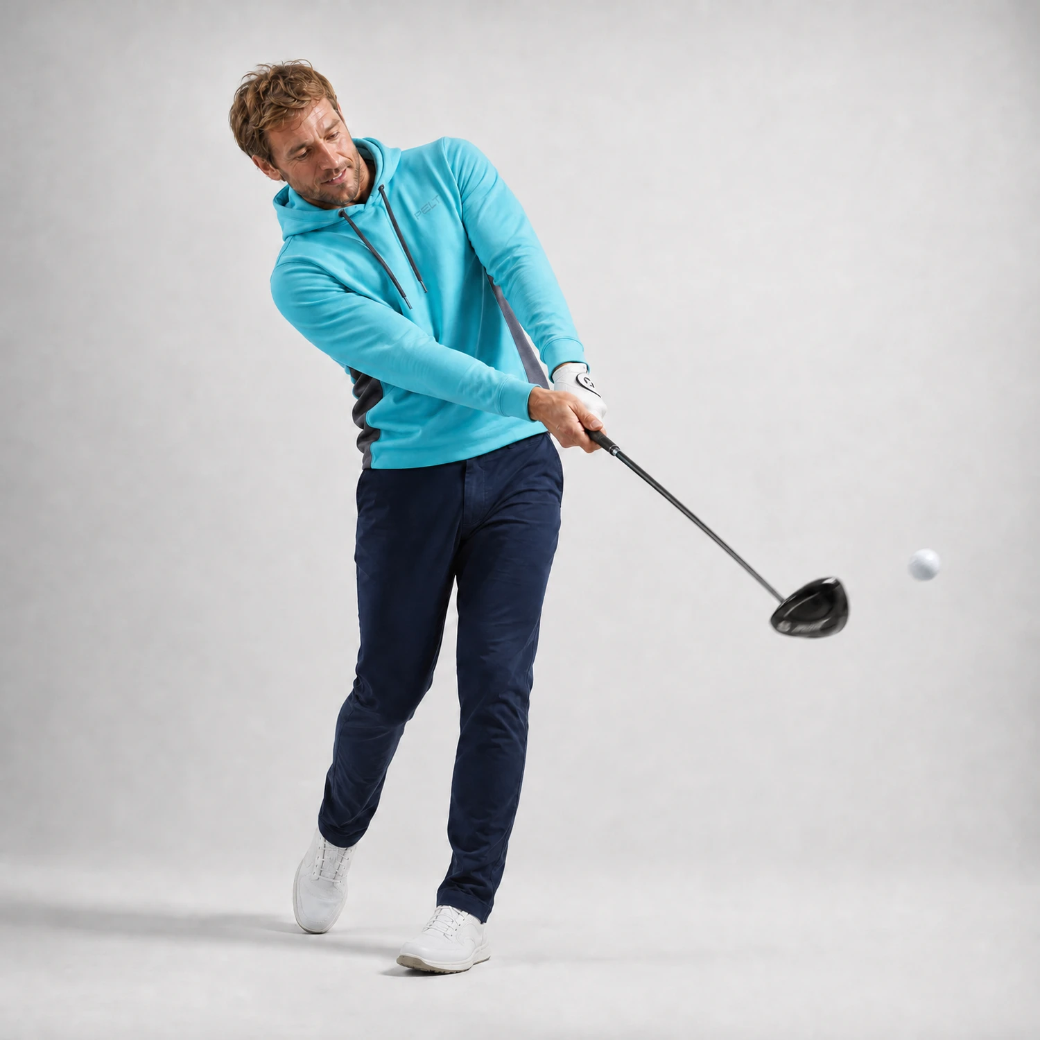 Golfer im türkisen PELT Hoodie beim Abschlag mit dem Driver